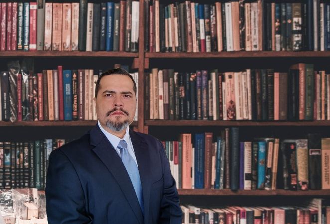 Homem de terno com livros ao fundo